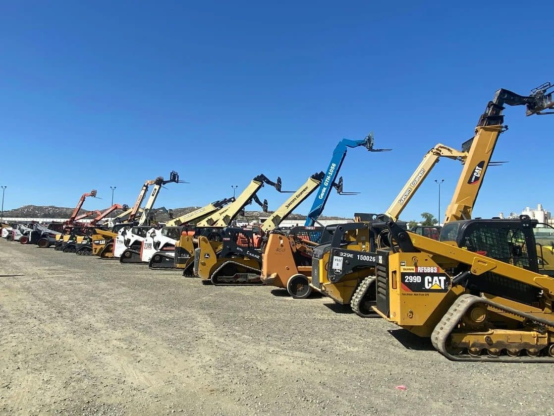 A row of skid-steer loaders and telehandlers lined up in an equipment yard