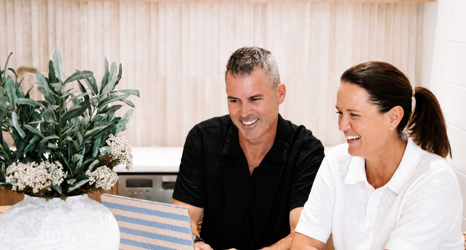 A couple going through their finance options together on a laptop at their kitchen bench