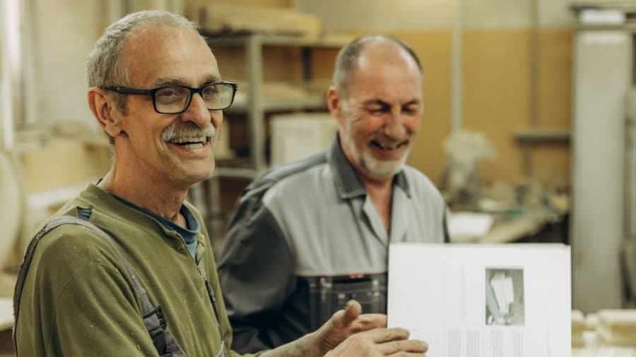 Two workshop owners laughing together over a set of plans on the factory floor